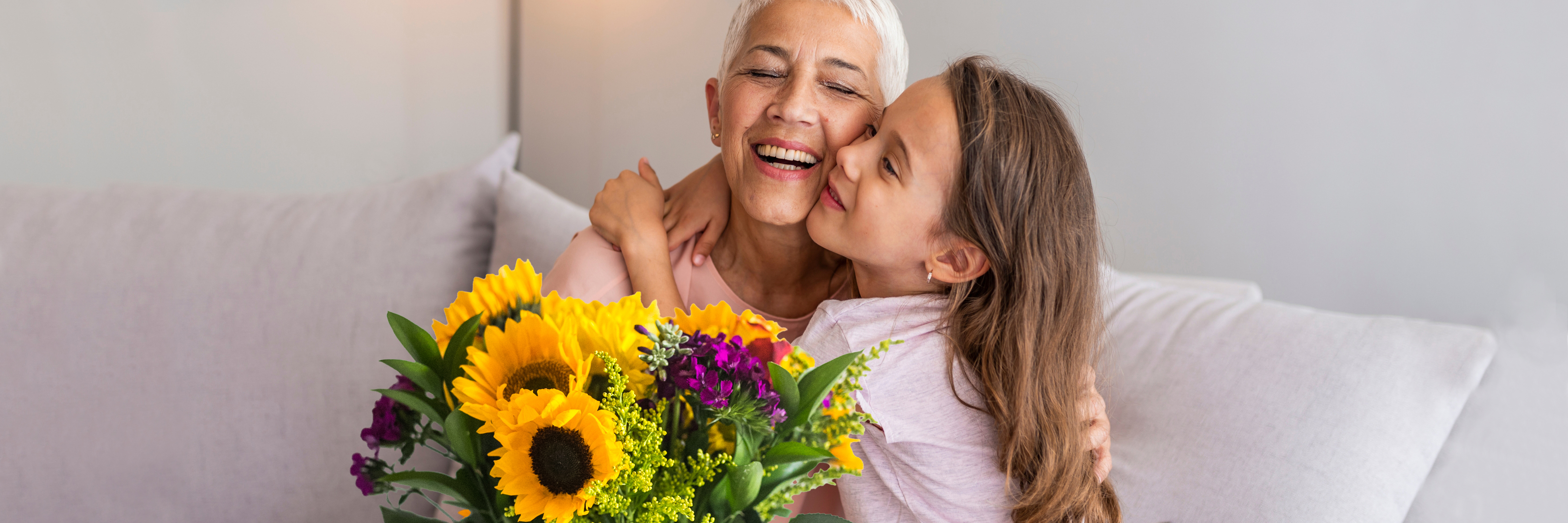 A cheerful older woman embraces a young girl, holding a vibrant sunflower bouquet, radiating joy.