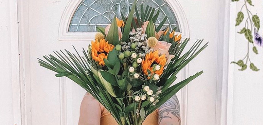 Bright floral bouquet featuring orange sunflowers, greenery, and delicate white blooms.