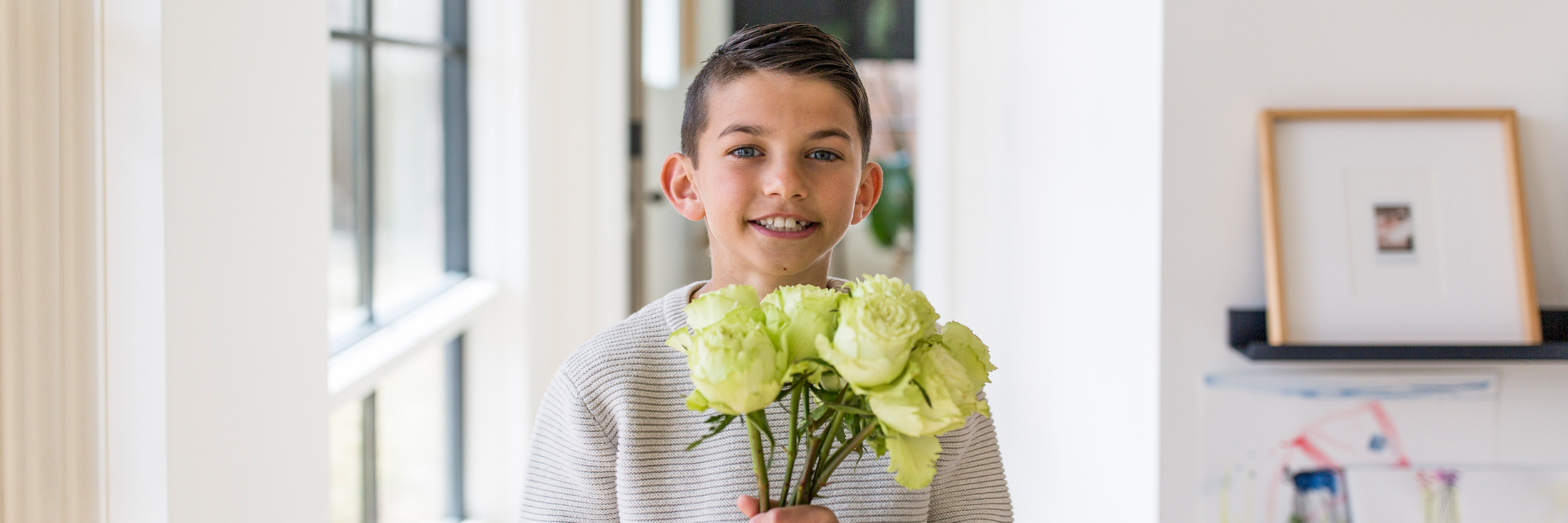 A cheerful young boy holding a bouquet of green roses, smiling in a bright interior.
