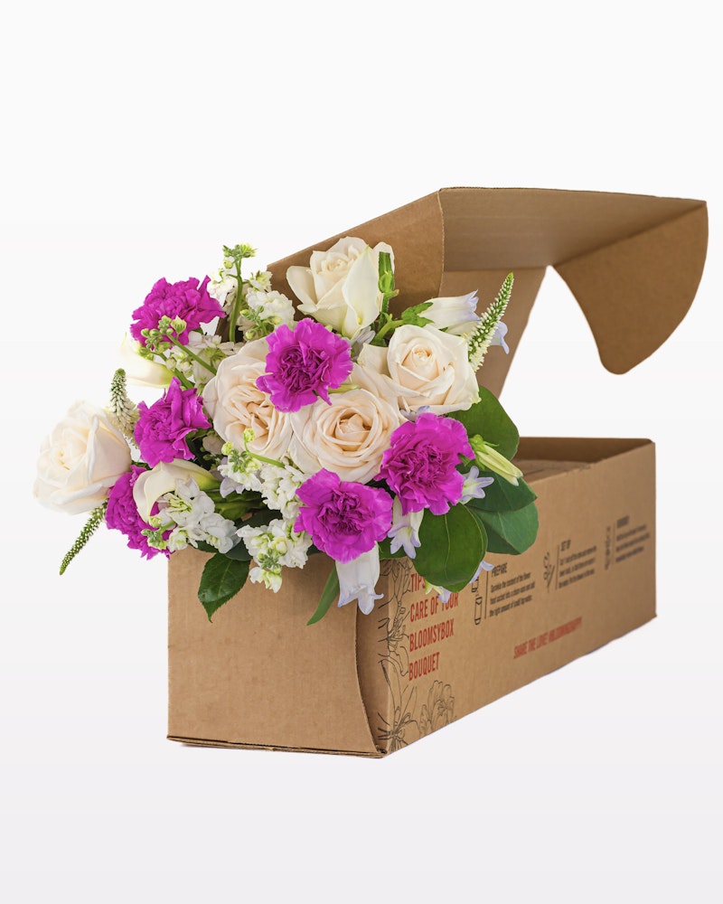 Beautiful bouquet of fresh flowers featuring roses and other blooms spilling out of a cardboard flower box designed for delivery, against an isolated white background.