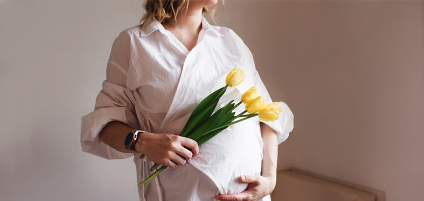A pregnant woman holds a bouquet of yellow tulips, radiating warmth and joy.