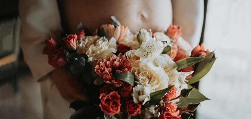 A beautiful floral bouquet featuring roses, carnations, and lush greenery, held gently.