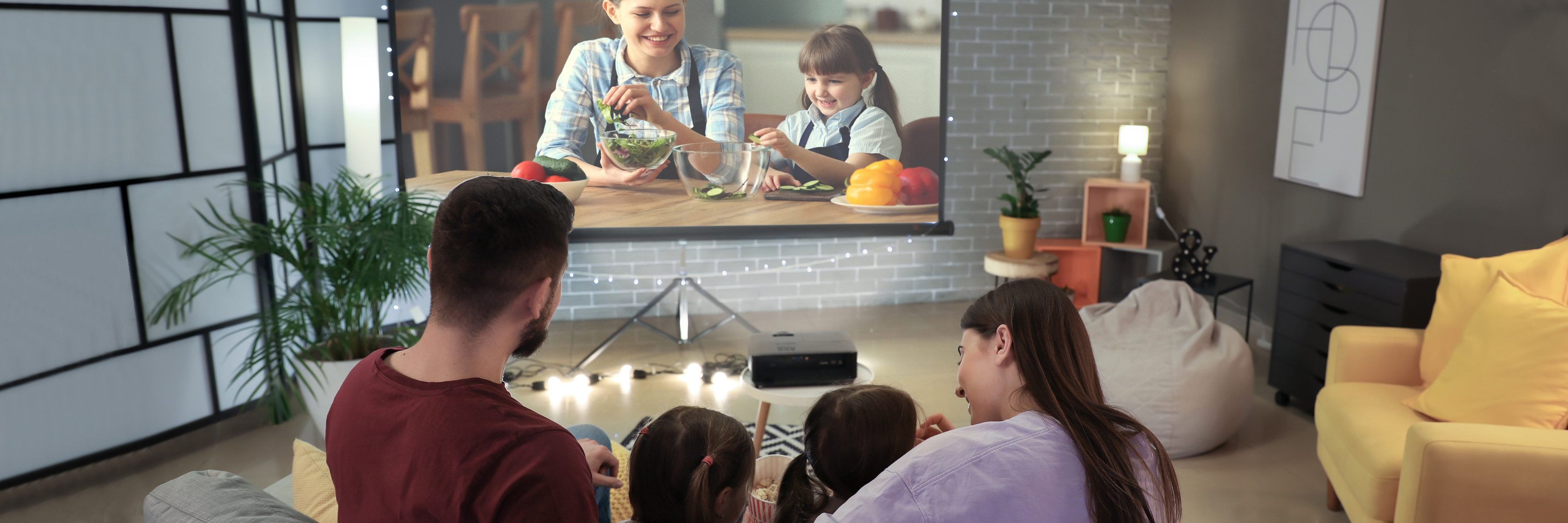 Family enjoying a movie night at home, watching a film projected on a large screen.