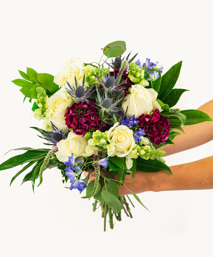 Elegant floral bouquet featuring white roses, vibrant purple blooms, and lush greenery.