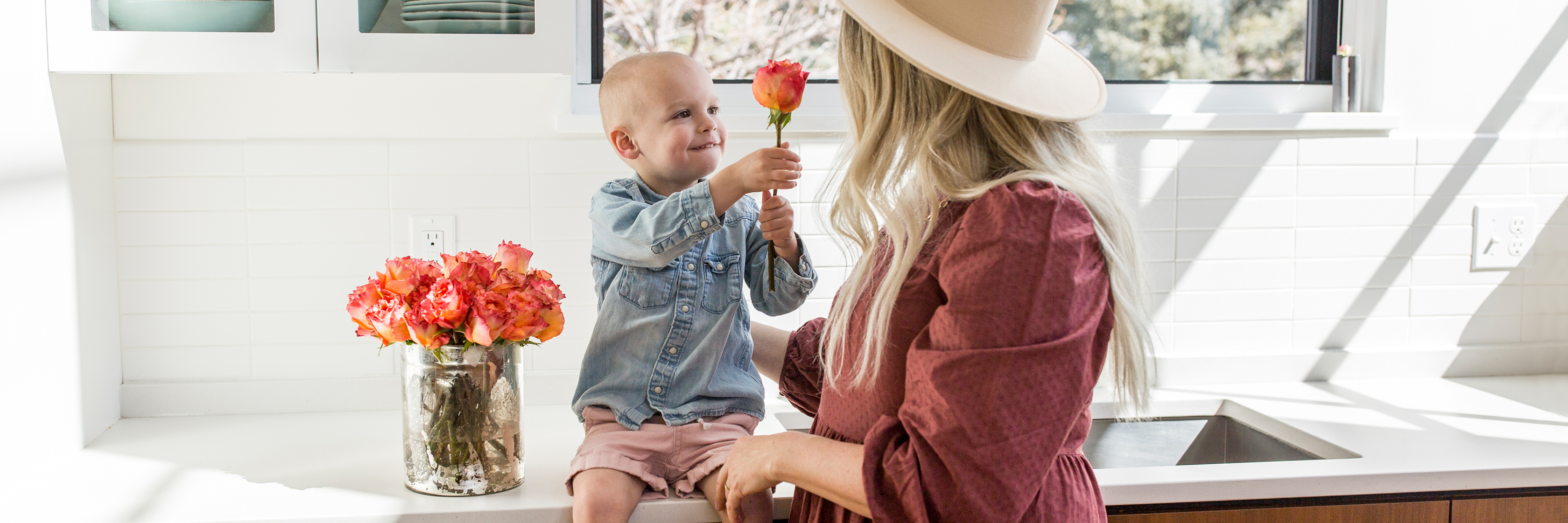 A joyful moment between a mother and son, sharing flowers in a bright kitchen.