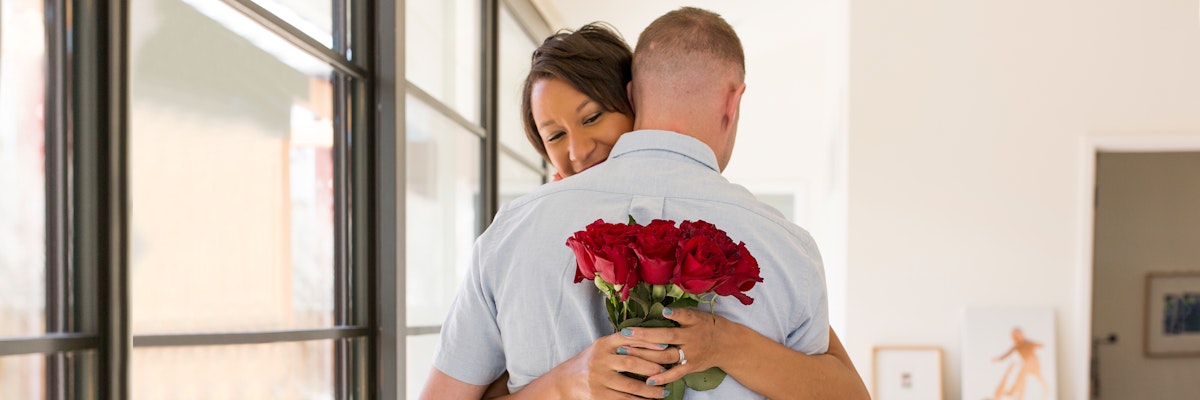 A couple sharing a warm embrace, featuring a romantic bouquet of red roses.