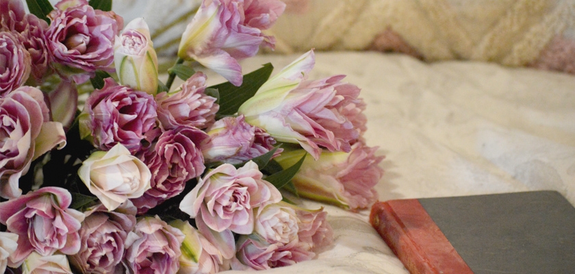 Delicate bouquet of pink tulips and roses beside a vintage book on a cozy background.