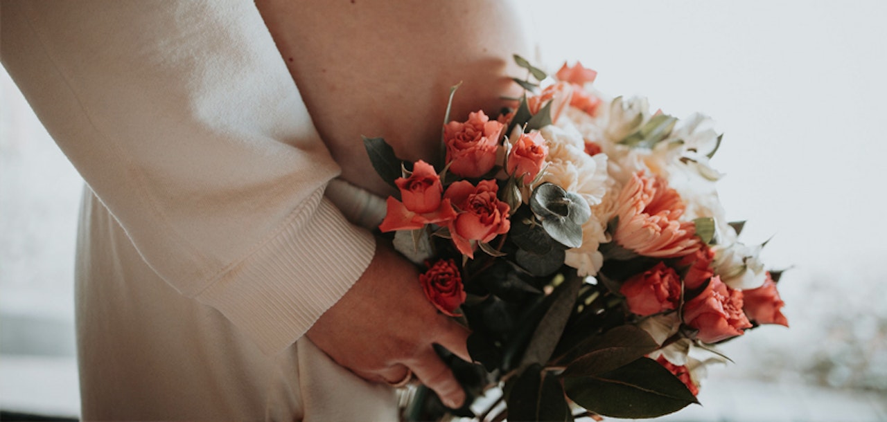A person in a light-colored outfit holding a beautiful bouquet of red roses and white flowers, suggesting a romantic or celebratory occasion like a wedding or anniversary.