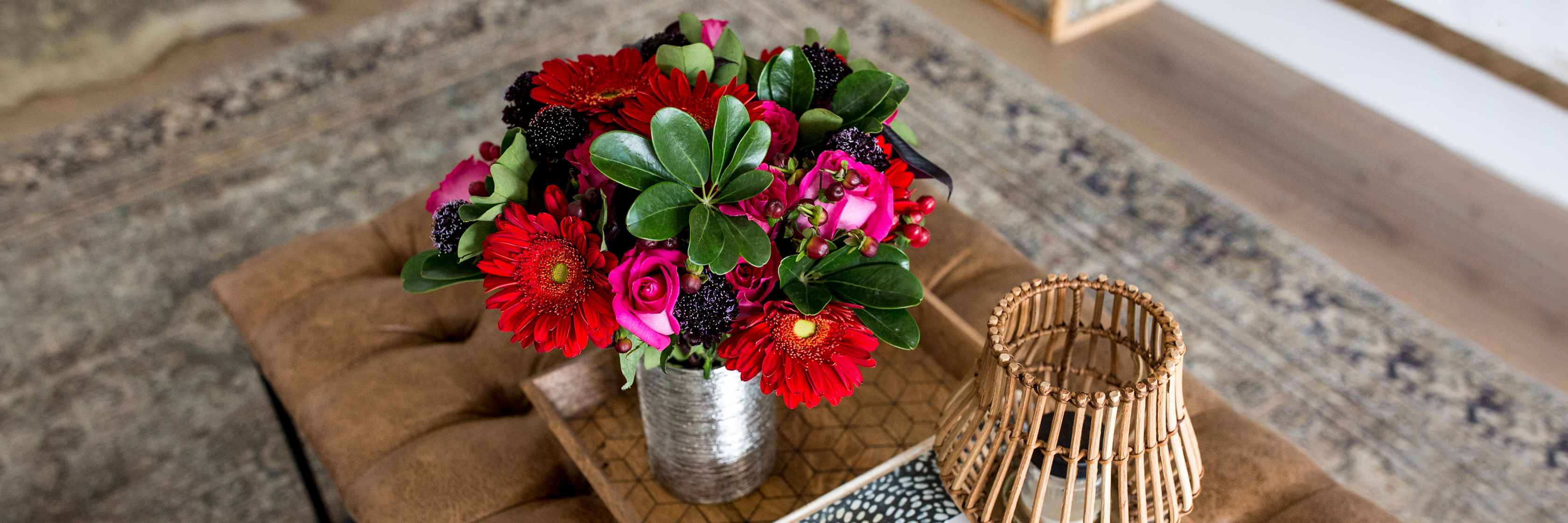 Vibrant floral arrangement featuring red gerbera daisies and roses in a stylish tin vase.