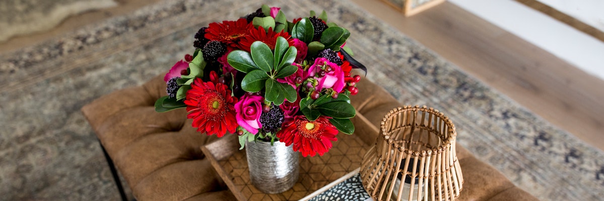 Vibrant floral arrangement featuring red gerbera daisies and roses in a stylish tin vase.