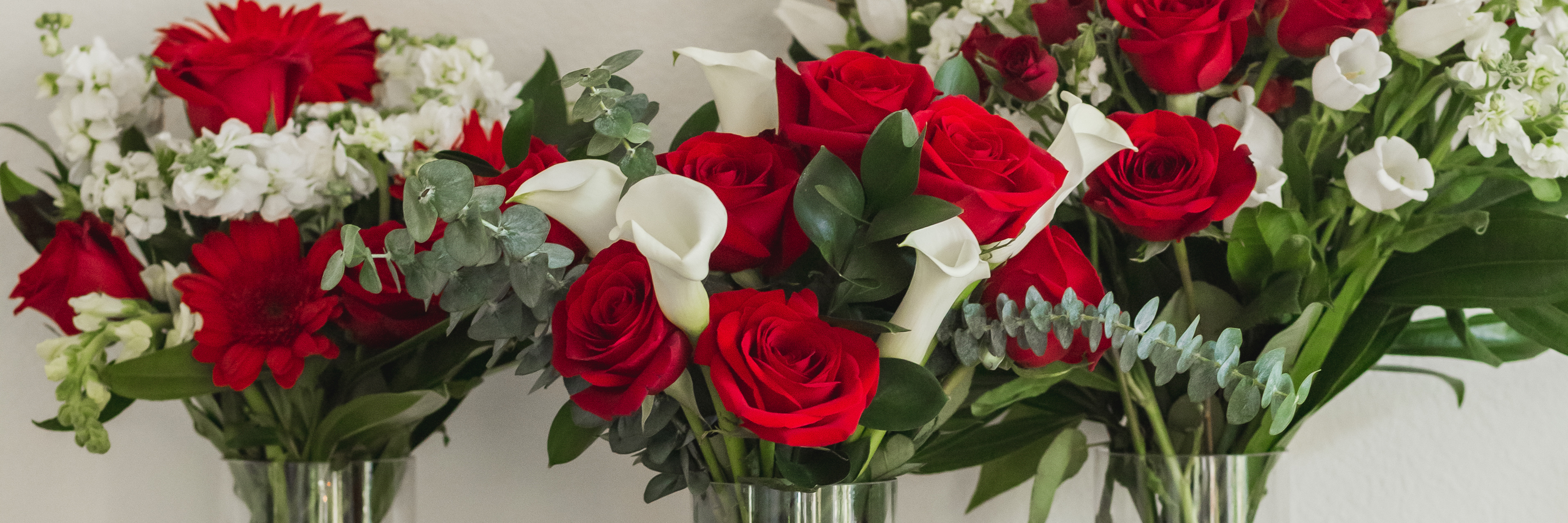 Vibrant floral display featuring red roses, calla lilies, and white blooms in elegant vases.