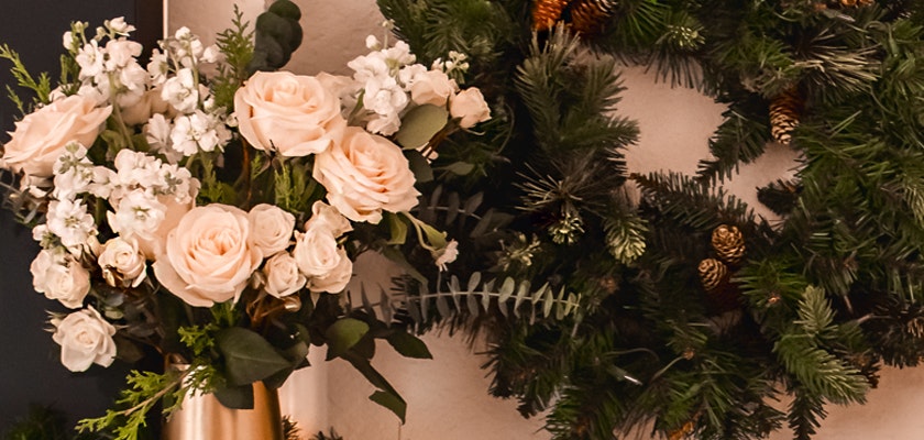 Elegant blush roses and white blooms in a stylish vase, complemented by a festive green wreath.