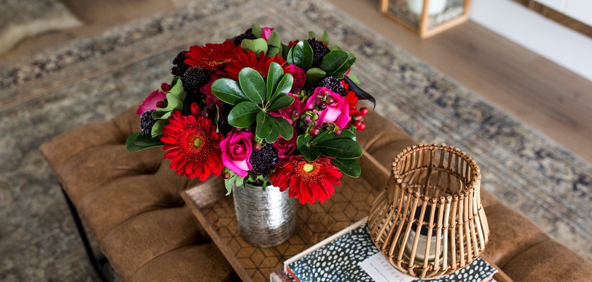 Vibrant floral arrangement featuring red gerbera daisies, roses, and lush greenery in a chic vase.