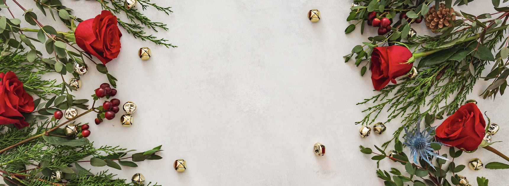 Festive arrangement of red roses, greenery, and gold bells, perfect for holiday celebrations.