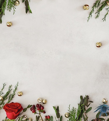 Festive arrangement of greenery and red roses with golden bells for holiday decor.