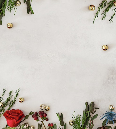 Festive arrangement of greenery and red roses with golden bells for holiday decor.