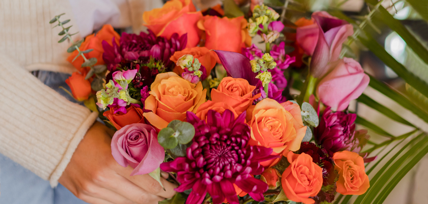 Vibrant floral bouquet featuring pink and orange roses, chrysanthemums, and lush greenery.