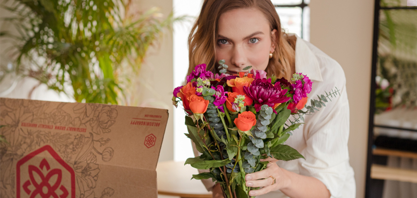 A woman joyfully holds a vibrant bouquet of mixed flowers while standing near a decorative box.