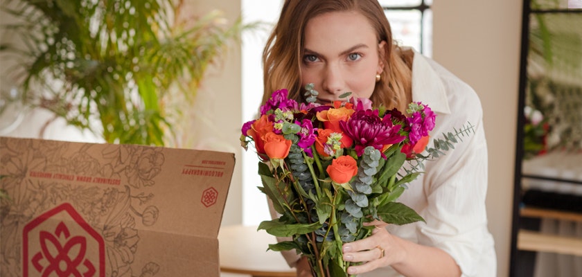 A woman joyfully holds a vibrant bouquet of mixed flowers while standing near a decorative box.