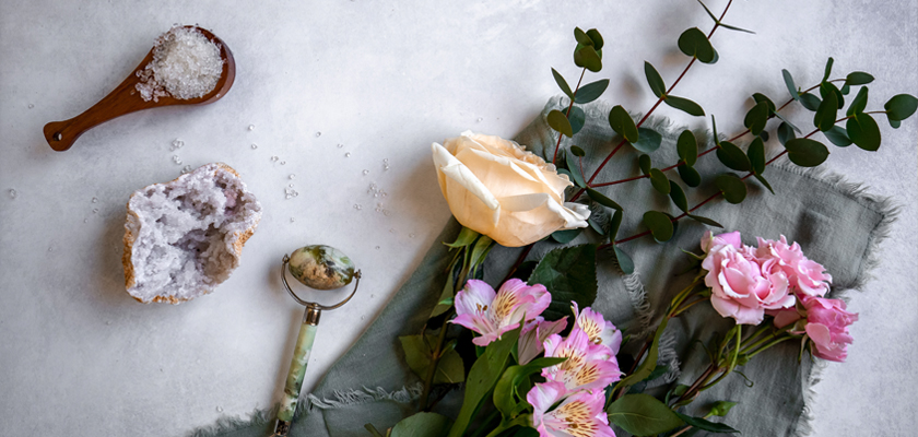 A serene flat lay featuring fresh flowers, salt crystals, and greenery on a soft fabric background.