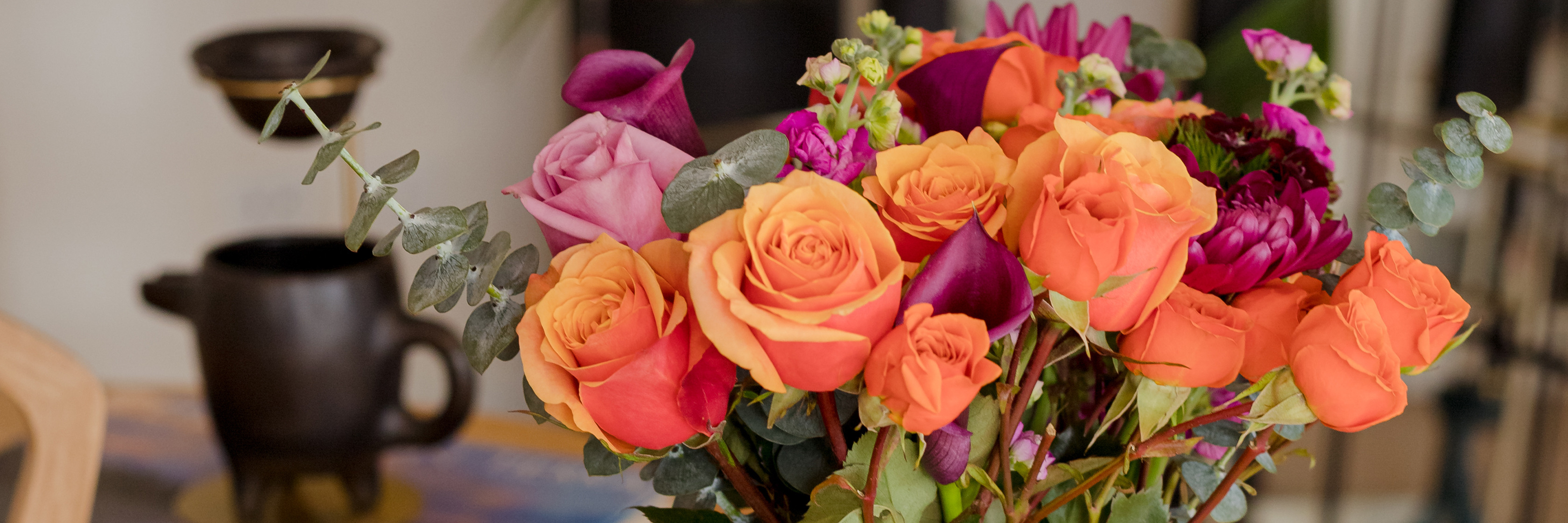 Vibrant floral arrangement of orange, pink, and purple roses accentuated with greenery.