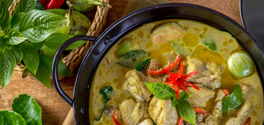 A flavorful chicken curry with fresh herbs and vibrant red chilies, served in a black pot.