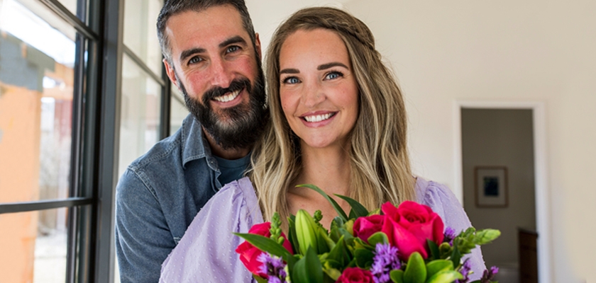 A happy couple poses indoors with a vibrant bouquet of flowers, celebrating love and joy.