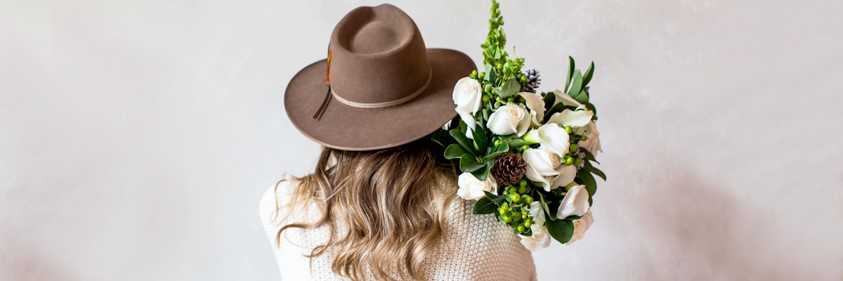 A woman in a wide-brimmed hat holding a lush floral bouquet of white and green blooms.