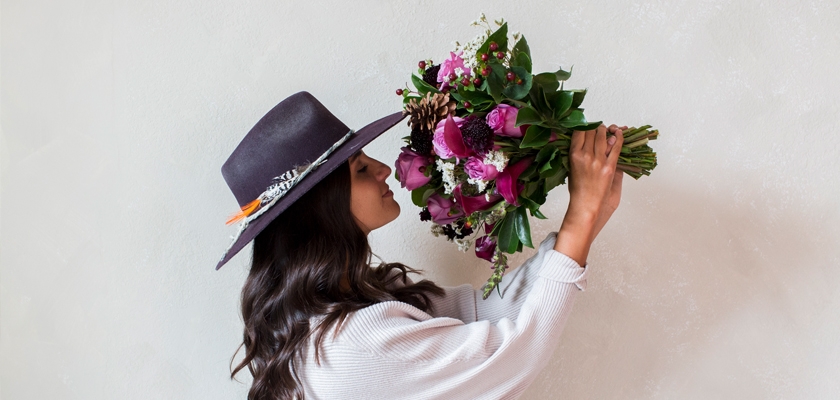 A woman in a stylish hat holds a vibrant bouquet of flowers close, showcasing its beauty.