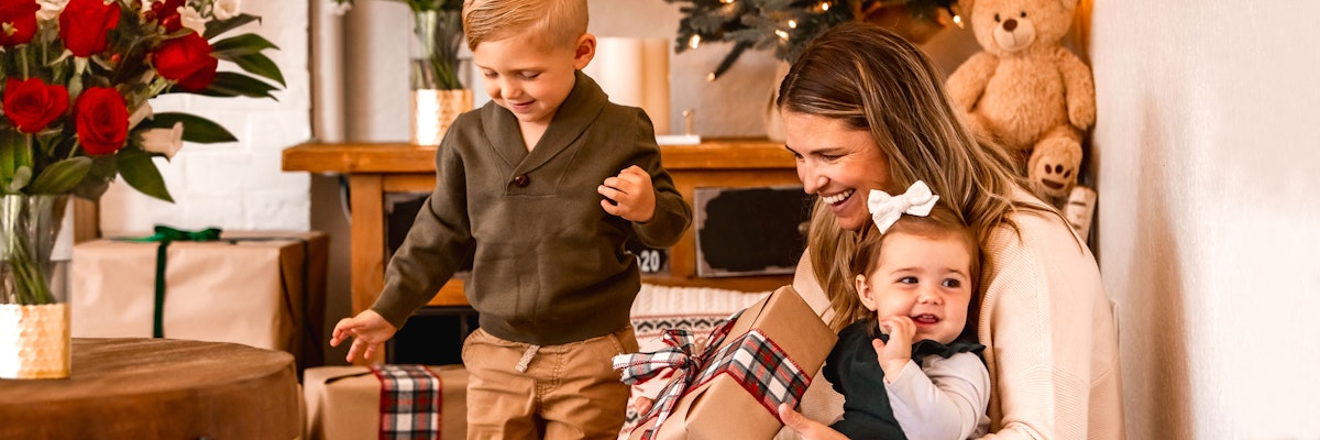 A joyful family moment with a mother and her kids, surrounded by holiday gifts and flowers.