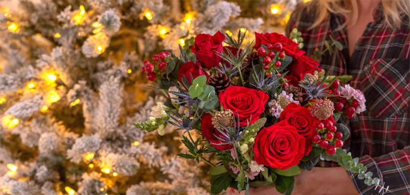 Festive floral arrangement of red roses and seasonal greenery, perfect for holiday celebrations.