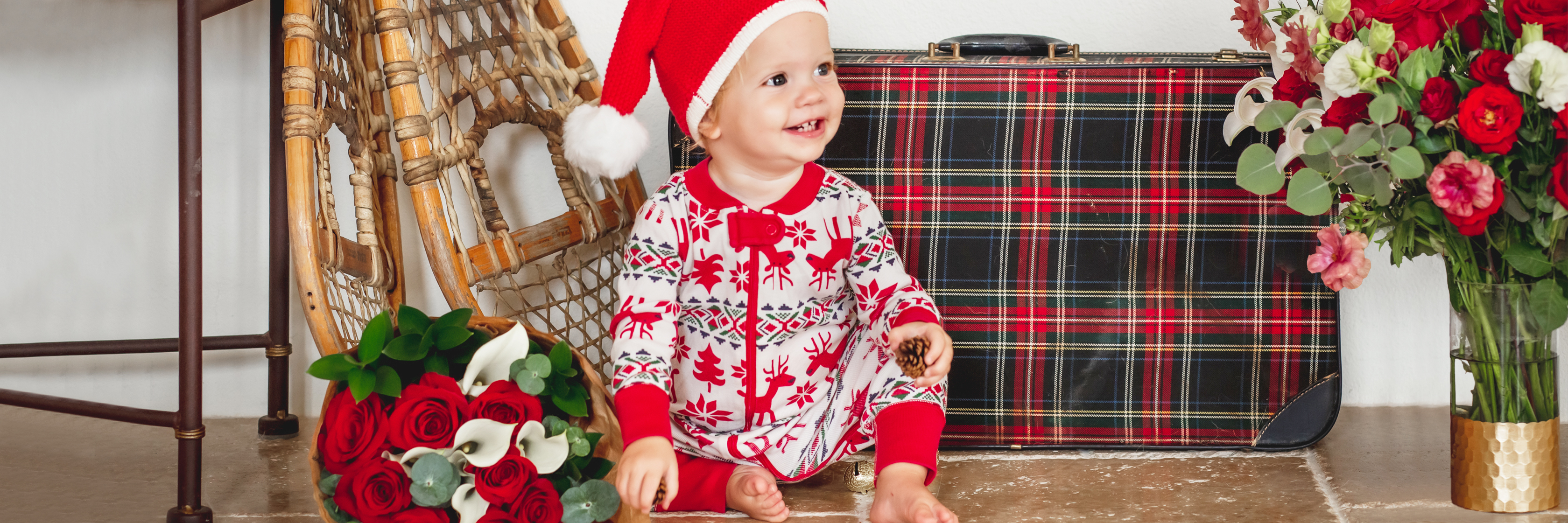 Adorable child in festive attire with a Christmas hat, surrounded by roses and holiday decor.