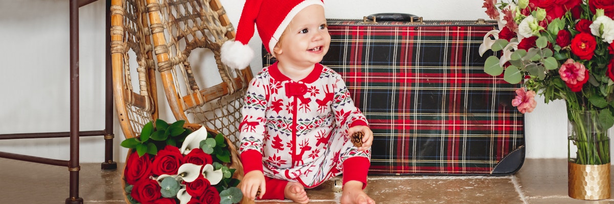 Adorable child in festive attire with a Christmas hat, surrounded by roses and holiday decor.