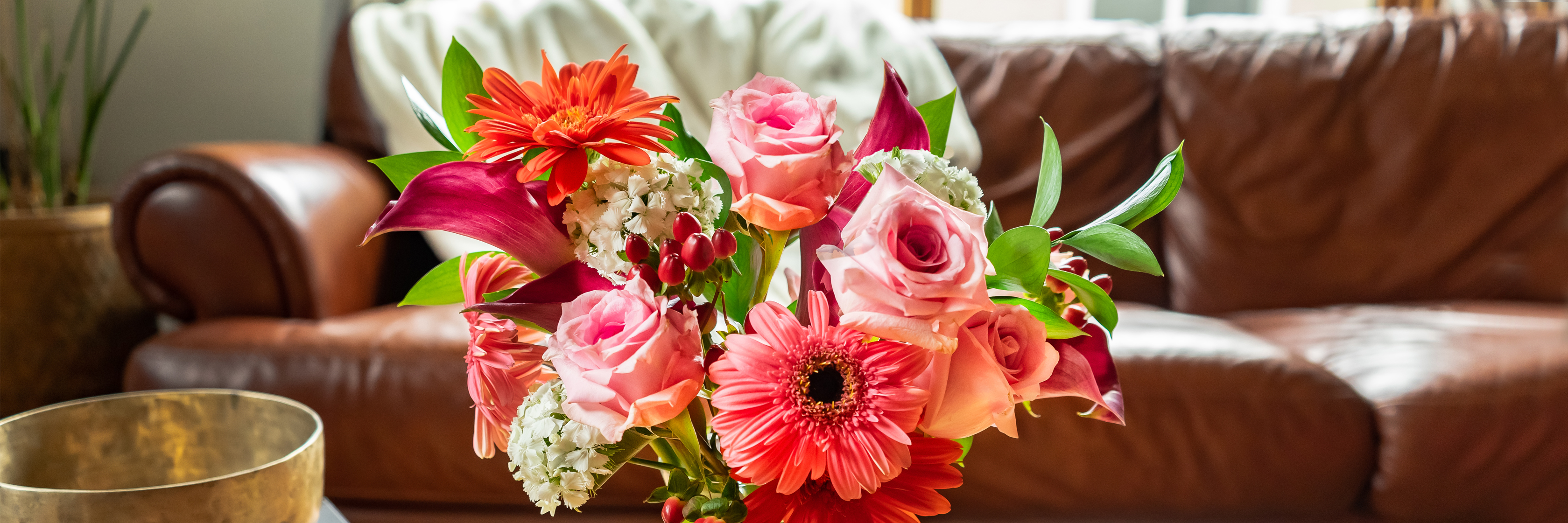 Vibrant floral arrangement featuring pink roses, gerbera daisies, and lilies in a cozy living room.