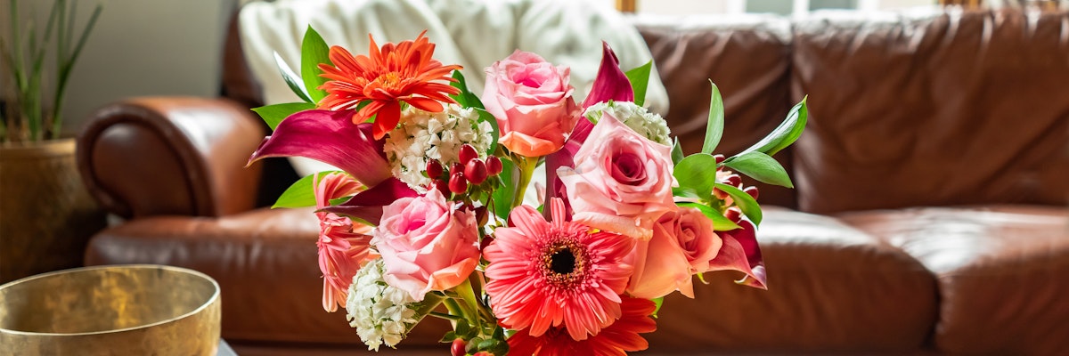Vibrant floral arrangement featuring pink roses, gerbera daisies, and lilies in a cozy living room.
