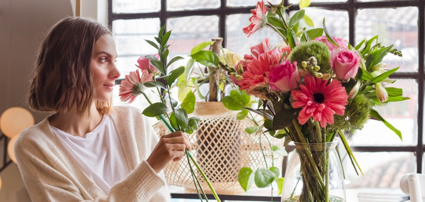 A woman carefully arranging a vibrant floral bouquet with pink gerbera daisies and roses.