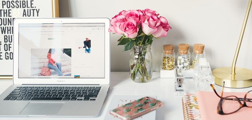 A stylish workspace featuring pink roses, a laptop, and chic stationery accessories.