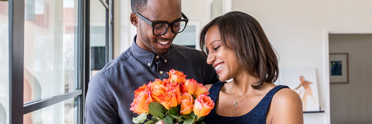 Happy couple joyfully sharing a bouquet of orange roses, celebrating love and connection.