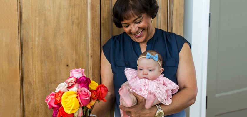 A joyful woman holds a baby girl and a vibrant rose bouquet, radiating happiness and love.