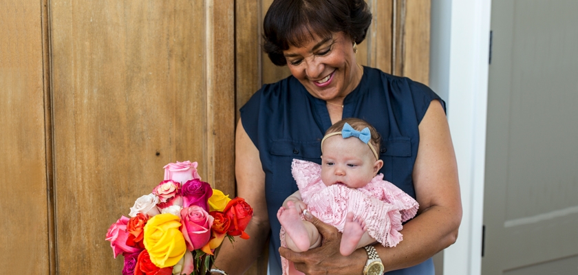 A joyful woman holds a baby girl and a vibrant rose bouquet, radiating happiness and love.