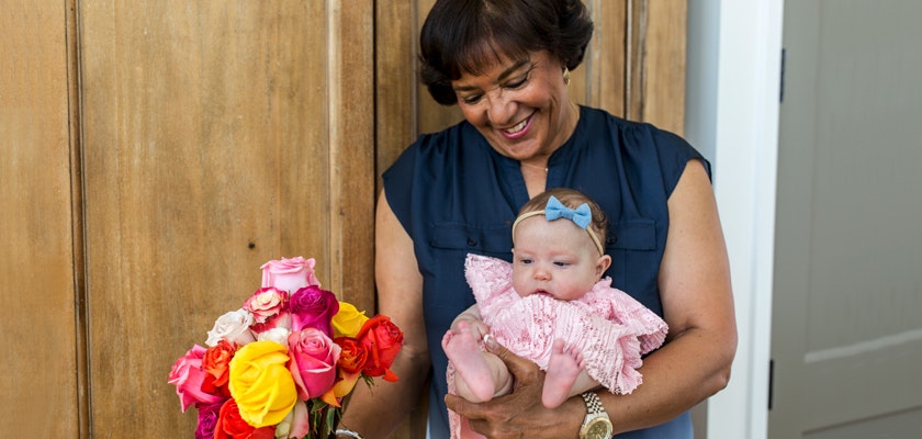 A joyful woman holds a baby girl and a vibrant rose bouquet, radiating happiness and love.
