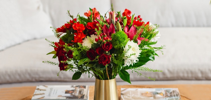 Vibrant mixed flower bouquet featuring red roses, lilies, and greenery in an elegant vase.