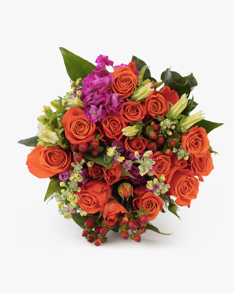 Vibrant bouquet of orange roses, purple flowers, and greenery with red berries against a white background, evoking warmth and joy in a floral arrangement.