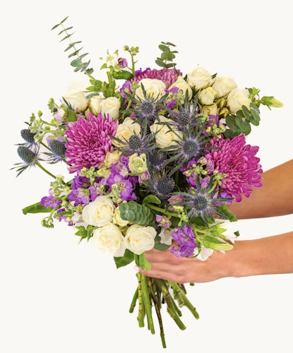 Vibrant floral arrangement featuring purple chrysanthemums and white roses in a hand-held bouquet.