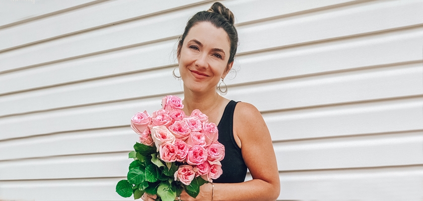 A smiling woman holding a vibrant bouquet of pink roses against a light backdrop.