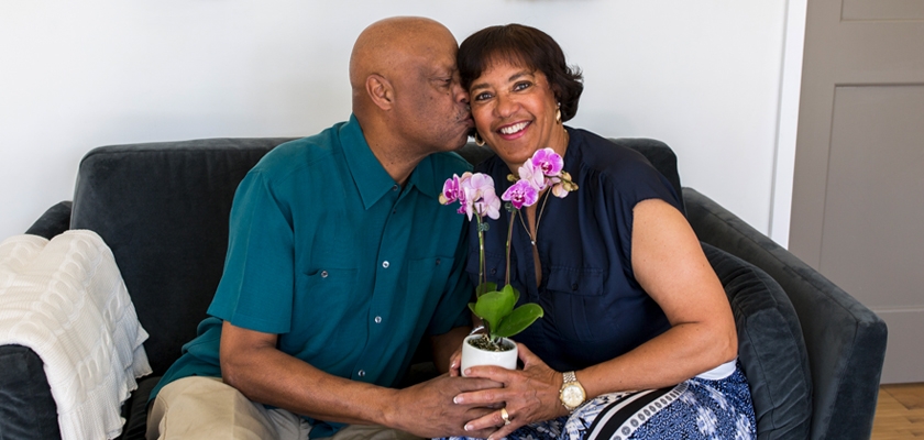 A joyful couple sharing a sweet moment on a couch, featuring a pot of orchids.