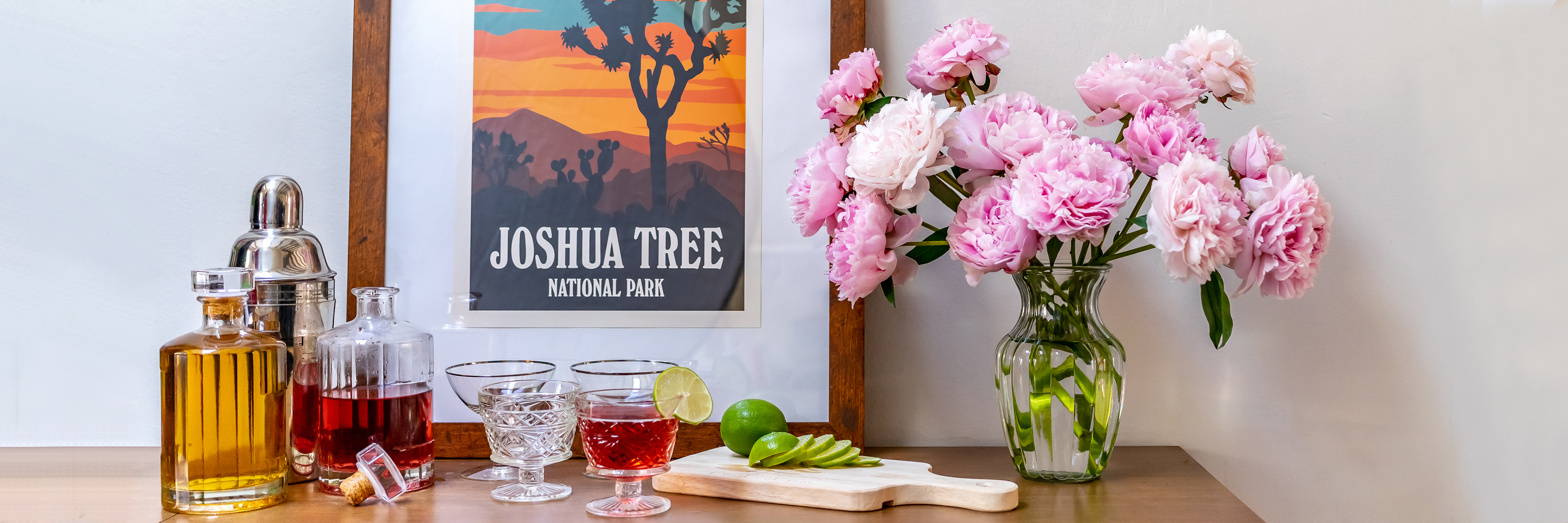Charming home bar setup featuring peonies, drinks, and a Joshua Tree poster.