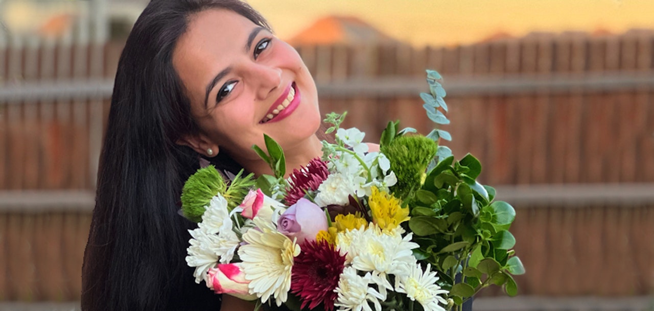 A cheerful woman holding a vibrant bouquet of mixed flowers, smiling brightly at sunset.