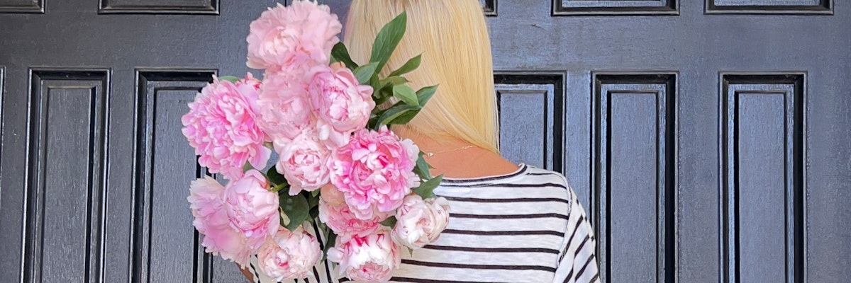 A woman holding a lush pink peony bouquet against a dark wooden door.