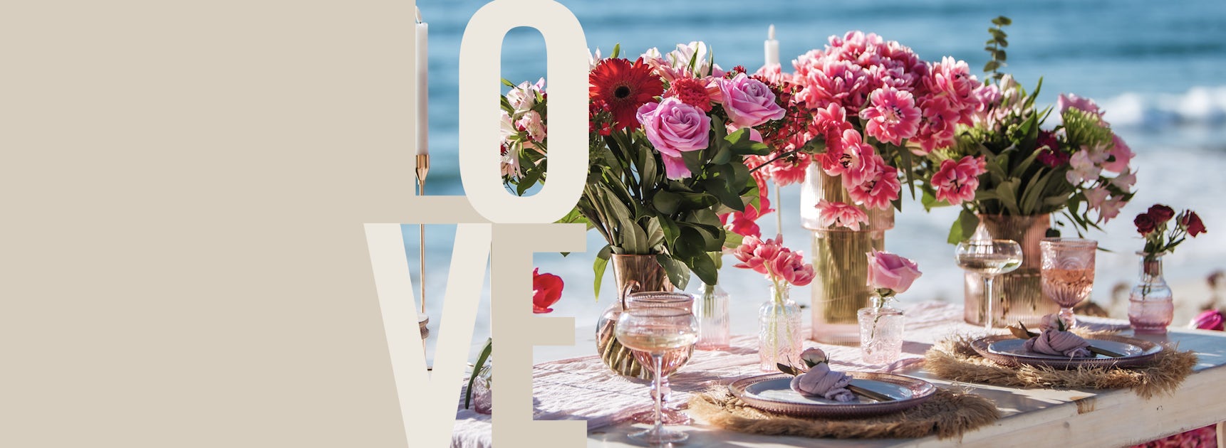 Elegant beachside table setting adorned with vibrant pink floral arrangements and fine dining wares.